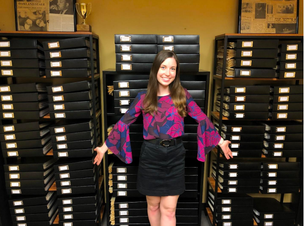 Emily Morris strikes a pose in front of the archives she spent the 2020-21 school year organizing. Thanks to her hard work, The Oakland Post archives are now accessible to the campus community.